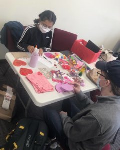 two ambassadors are at a table surrounded by craft materials while they work on making valentines